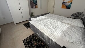 Ein Schlafzimmer mit einem Doppelbett, einem Kleiderschrank, einer Tür und zwei abstrakten Bildern an der Wand.