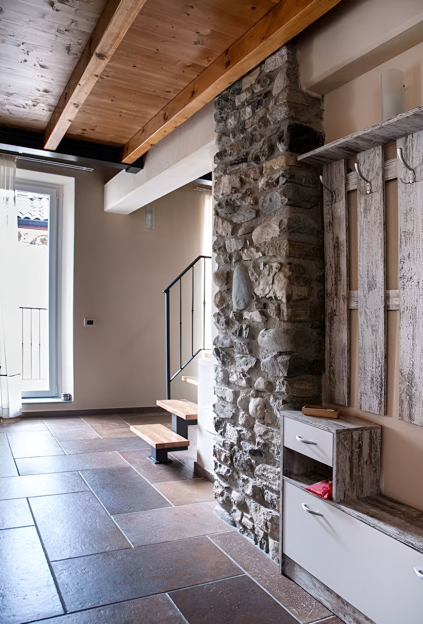 A modern interior with stone walls, wooden beams, and a staircase leading to an upper level.