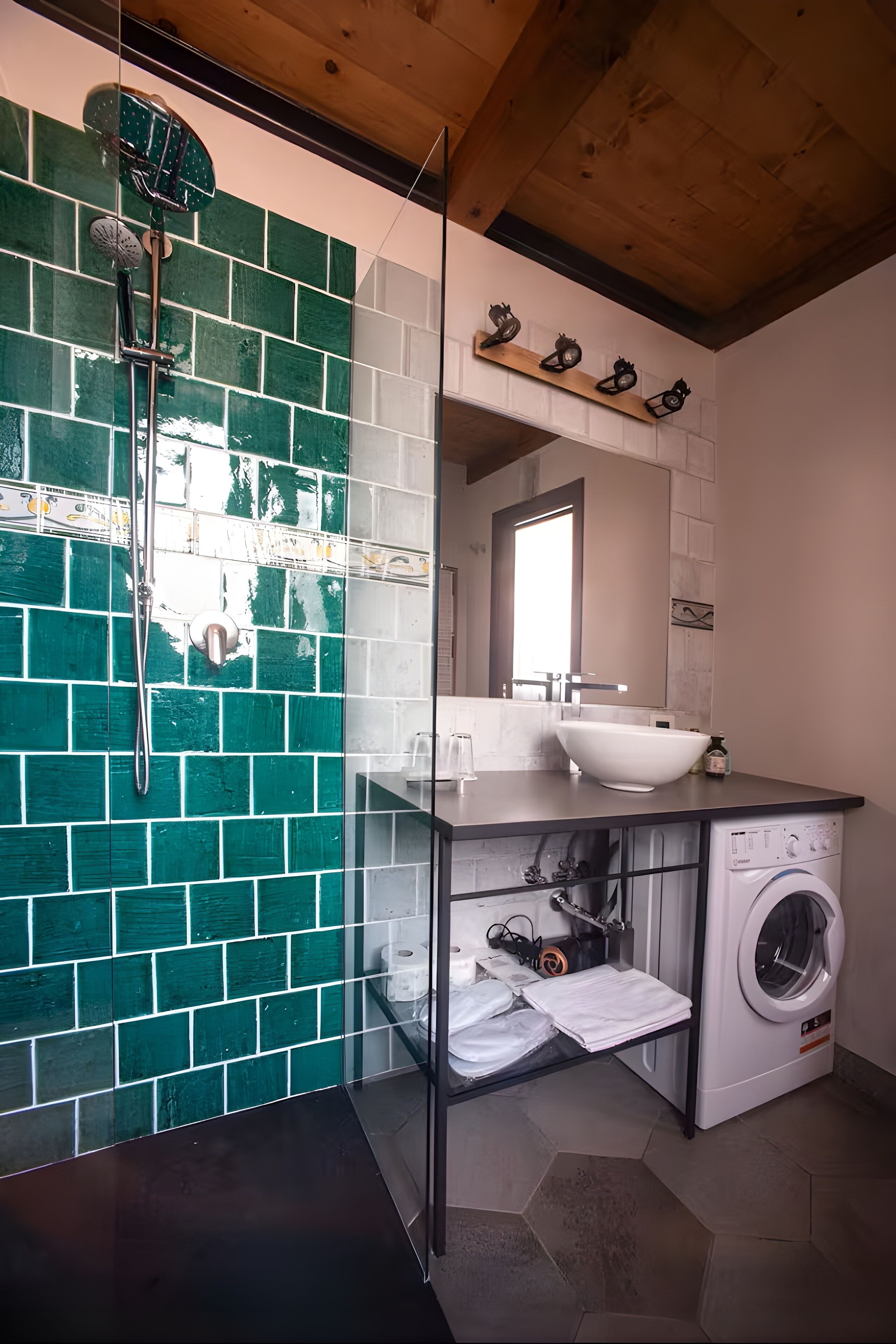 A modern bathroom with a green-tiled shower wall, a glass-enclosed washing machine, and a wooden ceiling.