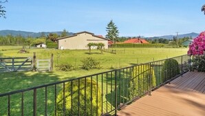 Une terrasse en bois avec une rambarde en métal, un terrain herbeux et un bâtiment avec un toit rouge.