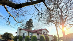 Une maison avec un toit rouge, entourée d’une pelouse bien entretenue et de plusieurs arbustes taillés.