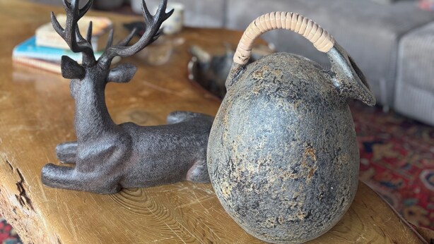 Un salon avec une table basse, une statuette de cerf décorative et un pichet en pierre.