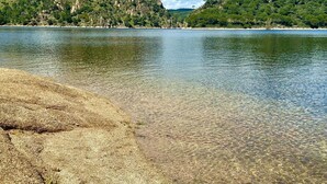 A clear lake with a rocky shore and hills in the background.