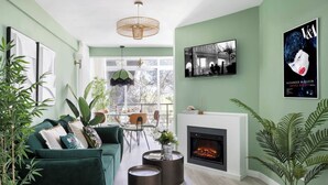A modern living room with a green sofa, a fireplace, and a dining area with a table and chairs.