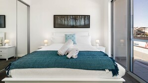 A modern hotel bedroom with a large bed, white bedding, a teal throw blanket, and a painting above the bed. - Casa Tranquilla - Short Walk to North Coogee Beach (North Coogee)