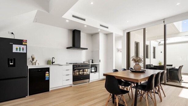 A modern kitchen with a central island, black appliances, and a dining area with a wooden table and black chairs. - Casa Tranquilla - Short Walk to North Coogee Beach (North Coogee)
