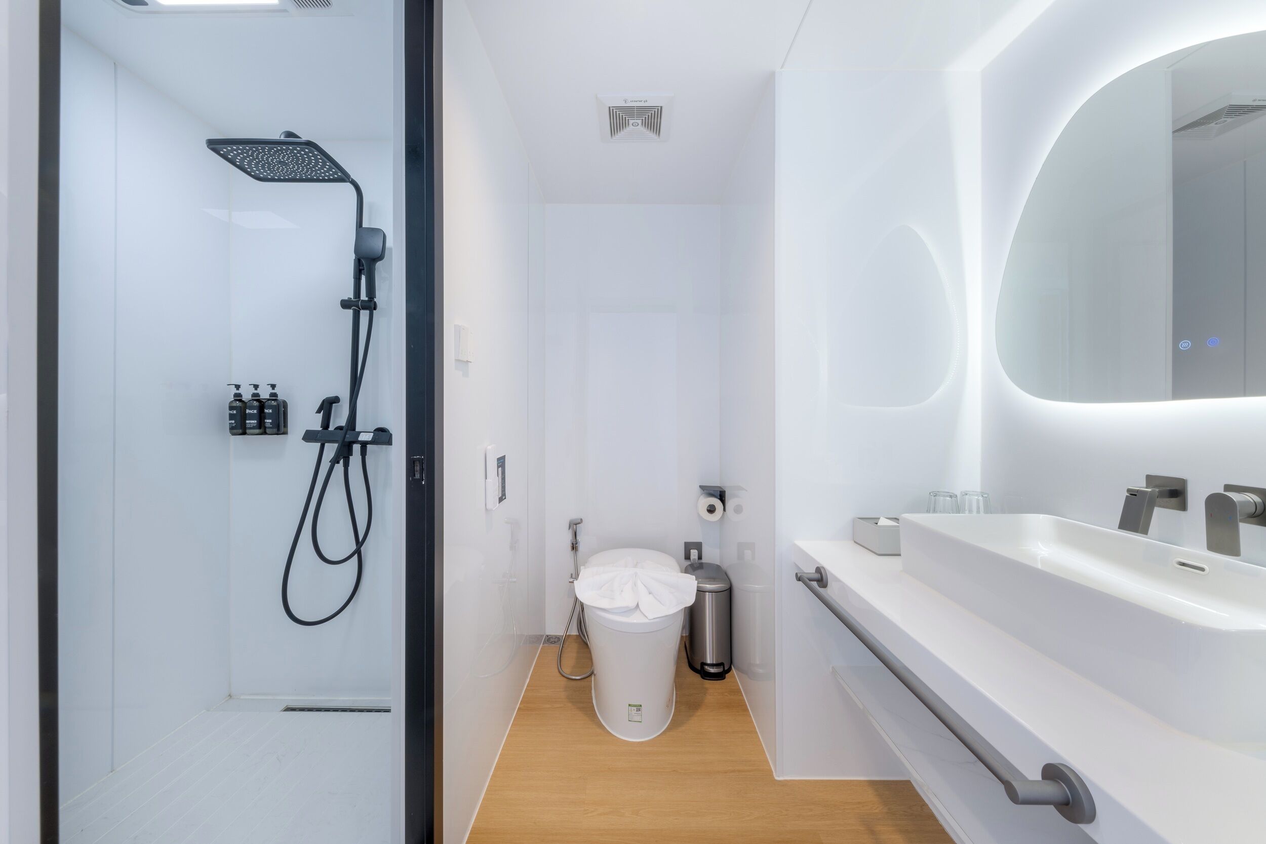 A modern bathroom with a glass shower enclosure, a white sink with a large mirror, and a toilet with a trash can.