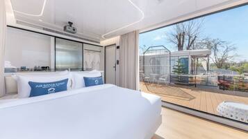 Una habitación de hotel moderna con una cama grande, un balcón con vistas al campo y una zona de ducha con paredes de vidrio.