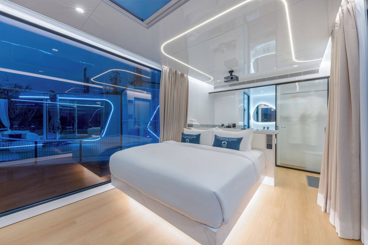 Een moderne hotelkamer met een groot bed, een glazen wand met uitzicht en een badkamer met douche en wastafel.
