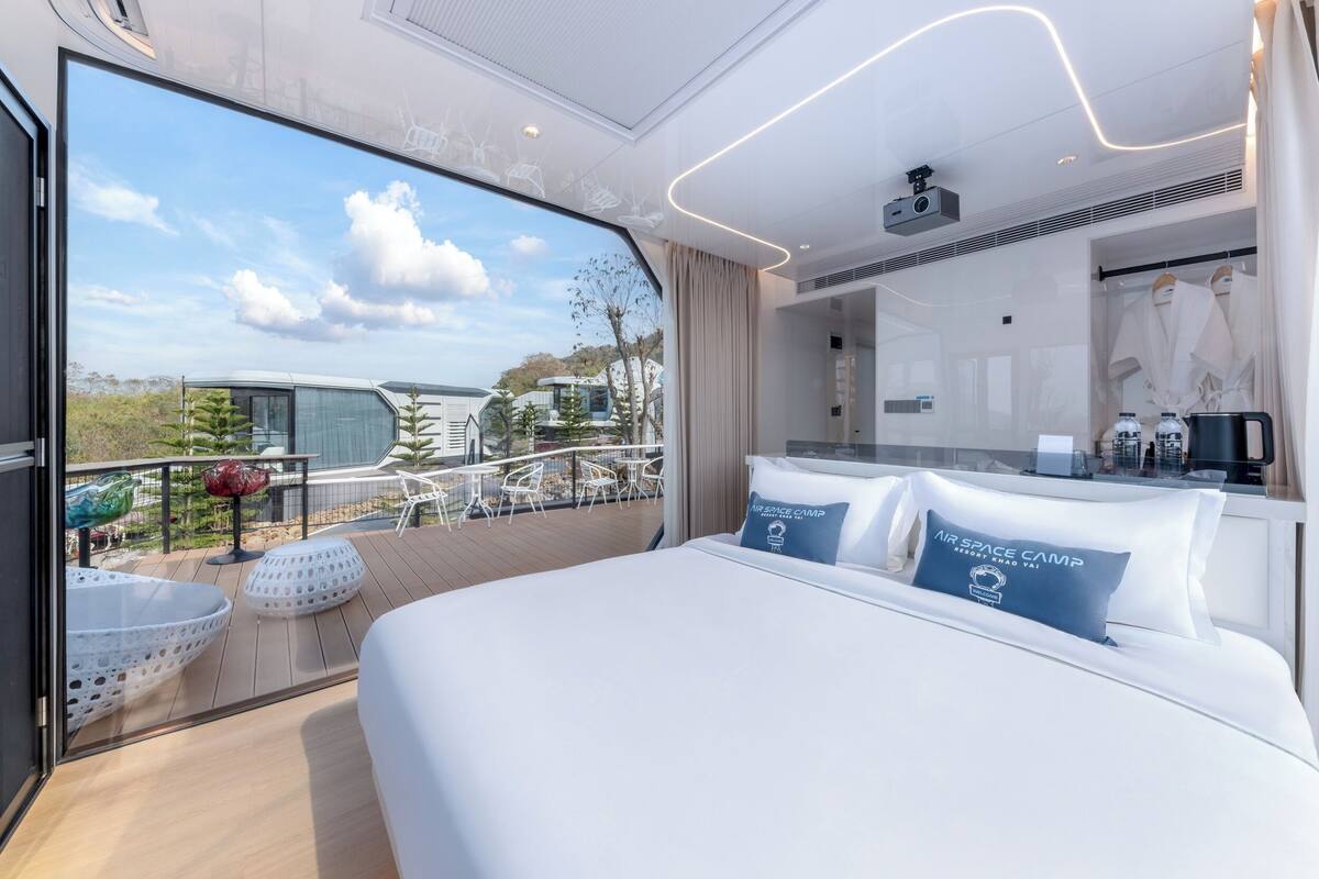Een moderne hotelkamer met een groot bed, een balkon met zitplaatsen buiten en uitzicht op de omgeving.