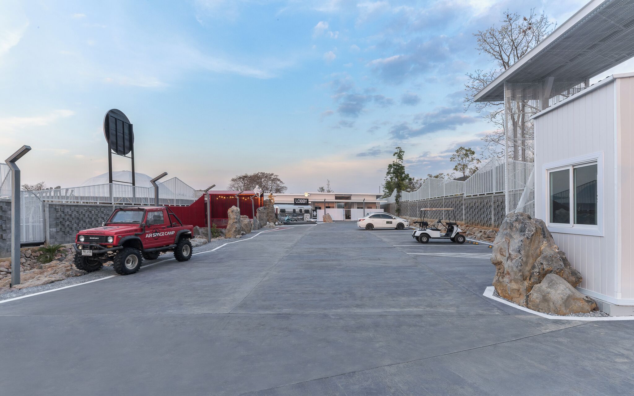 A parking area with a red SUV labeled "Air Space Camp" and a white car. There is a building with a sign that reads "Lobby" in the background.