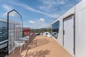 Una terraza en la azotea con sillas de metal blanco, una valla roja y vistas al paisaje.