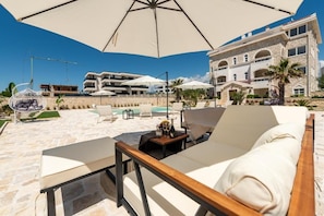 A sunlit outdoor seating area with a large umbrella, a pool, and a stone building in the background. - Chateau Dabo Luxury Pool Apartment (Novalja)