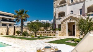 Uma área de piscina com espreguiçadeiras, uma mesa com bebidas e um edifício de pedra com arcos.