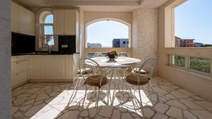 Uma cozinha moderna com armários brancos, uma mesa de jantar com cadeiras e uma janela grande com vista para edifícios.