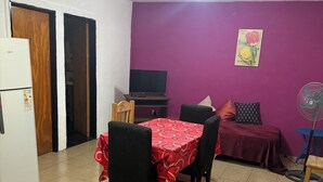 Un comedor con una mesa preparada para cuatro personas, un televisor y un ventilador.