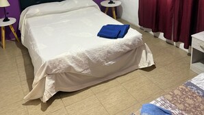 Un dormitorio con una cama, dos mesitas de noche, una lámpara, una ventana con cortinas y un cuadro en la pared.