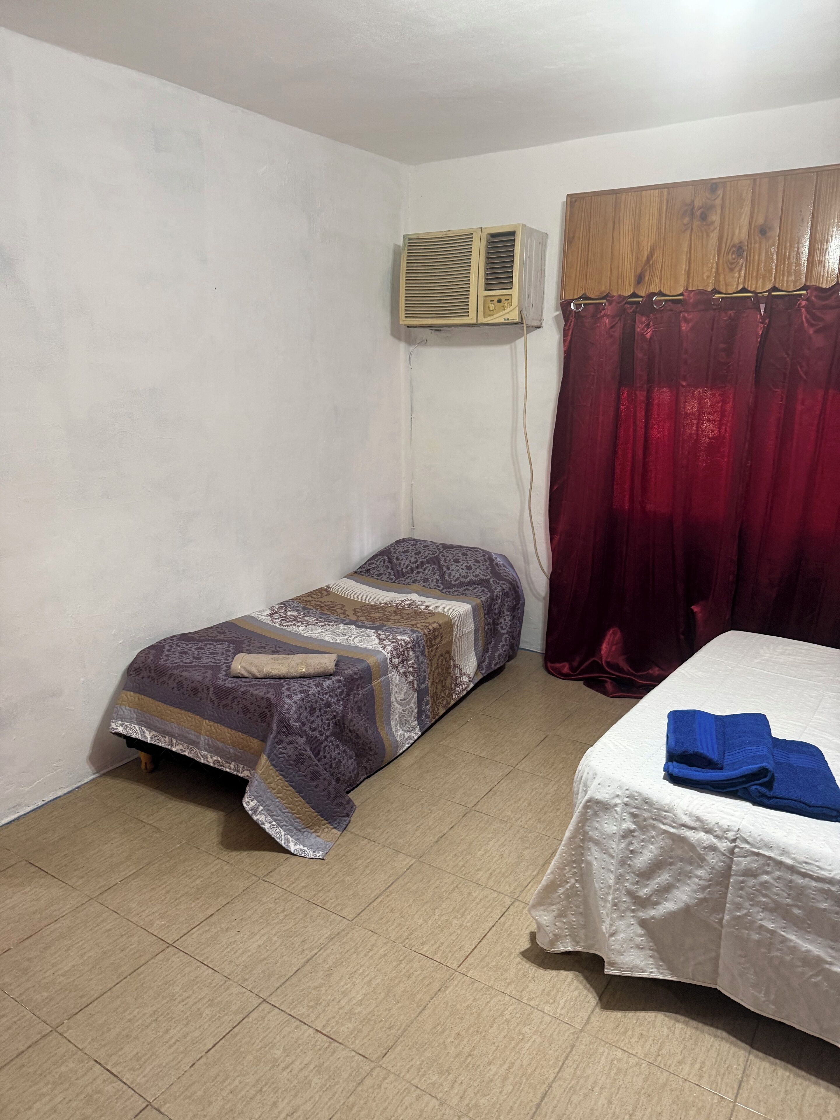Una habitación pequeña con una cama individual, una cama más pequeña, un armario de madera y un equipo de aire acondicionado.