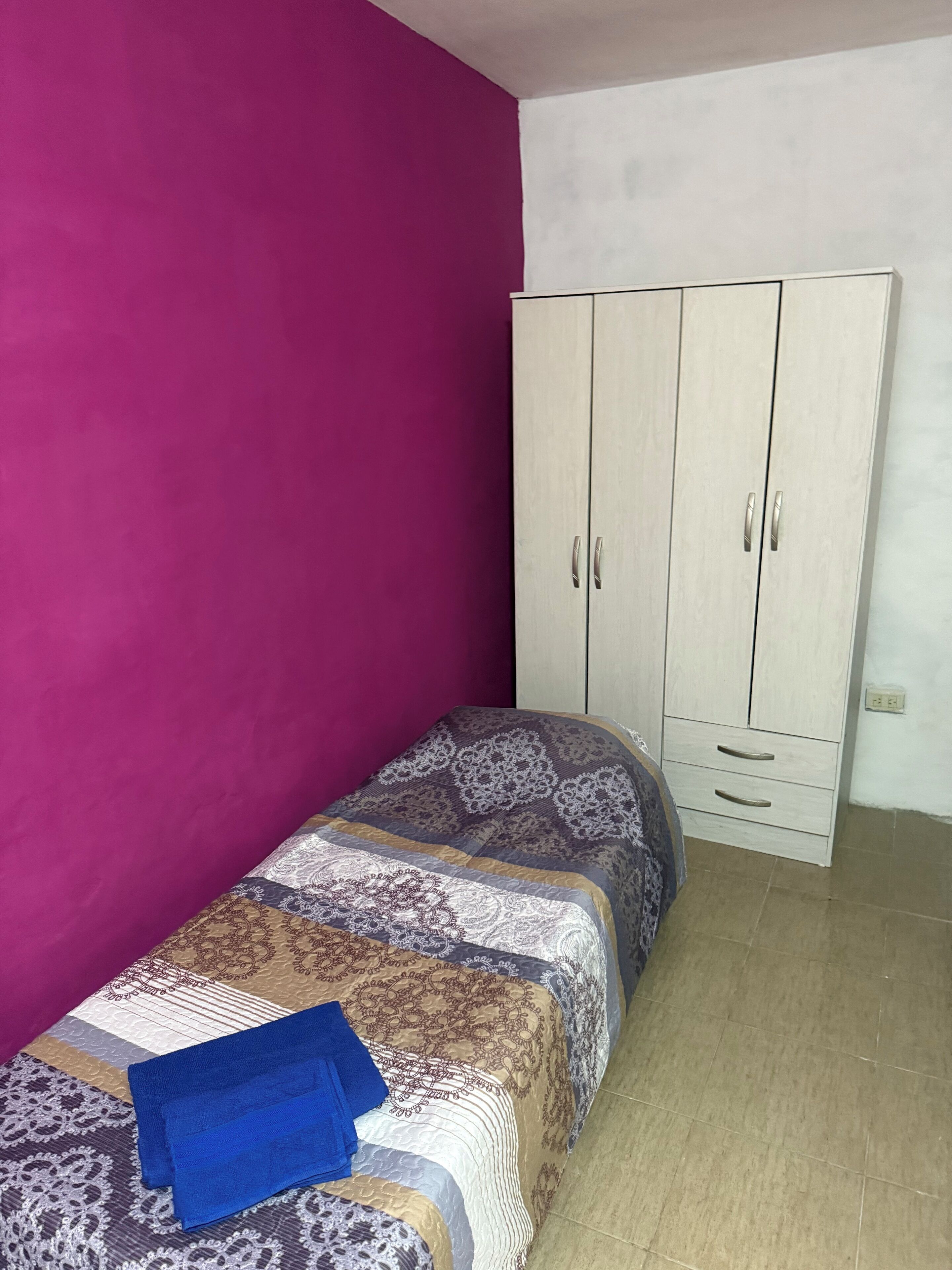 A bedroom with a bed, a wardrobe, and a purple wall.