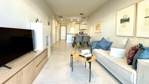 Ein modernes Wohnzimmer mit Flachbildfernseher, einer Couch mit Kissen, einem Couchtisch und gerahmten Bildern an der Wand.