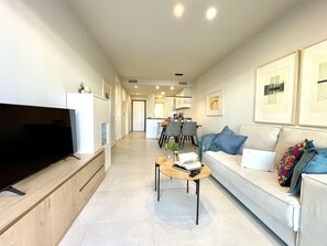 Ein modernes Wohnzimmer mit Flachbildfernseher, einer Couch mit Kissen, einem Couchtisch und gerahmten Bildern an der Wand.