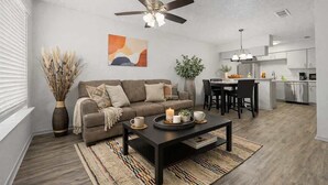 Ein modernes Wohnzimmer mit Sofa, Couchtisch und Essbereich, im Hintergrund eine Küche.