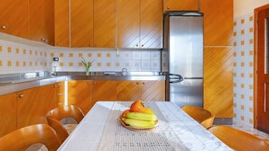 Una cocina moderna con armarios de madera, un refrigerador de acero inoxidable y una mesa de comedor con una cesta de frutas.