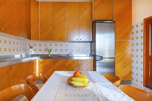 Eine moderne Küche mit Holzschränken, einem Edelstahlkühlschrank und einem Esstisch mit Obstkorb.