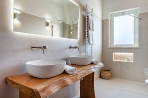 Ein modernes Badezimmer mit zwei großen weißen Waschbecken, einem Holzwaschtisch, einem großen Spiegel, einem Handtuchhalter und einem Fenster.