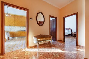 Un pasillo con un banco, un espejo y puertas que dan a un dormitorio y una cocina.