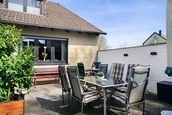 Une terrasse extérieure avec une table et des chaises, un pot de fleurs et une fenêtre donnant sur la cour.
