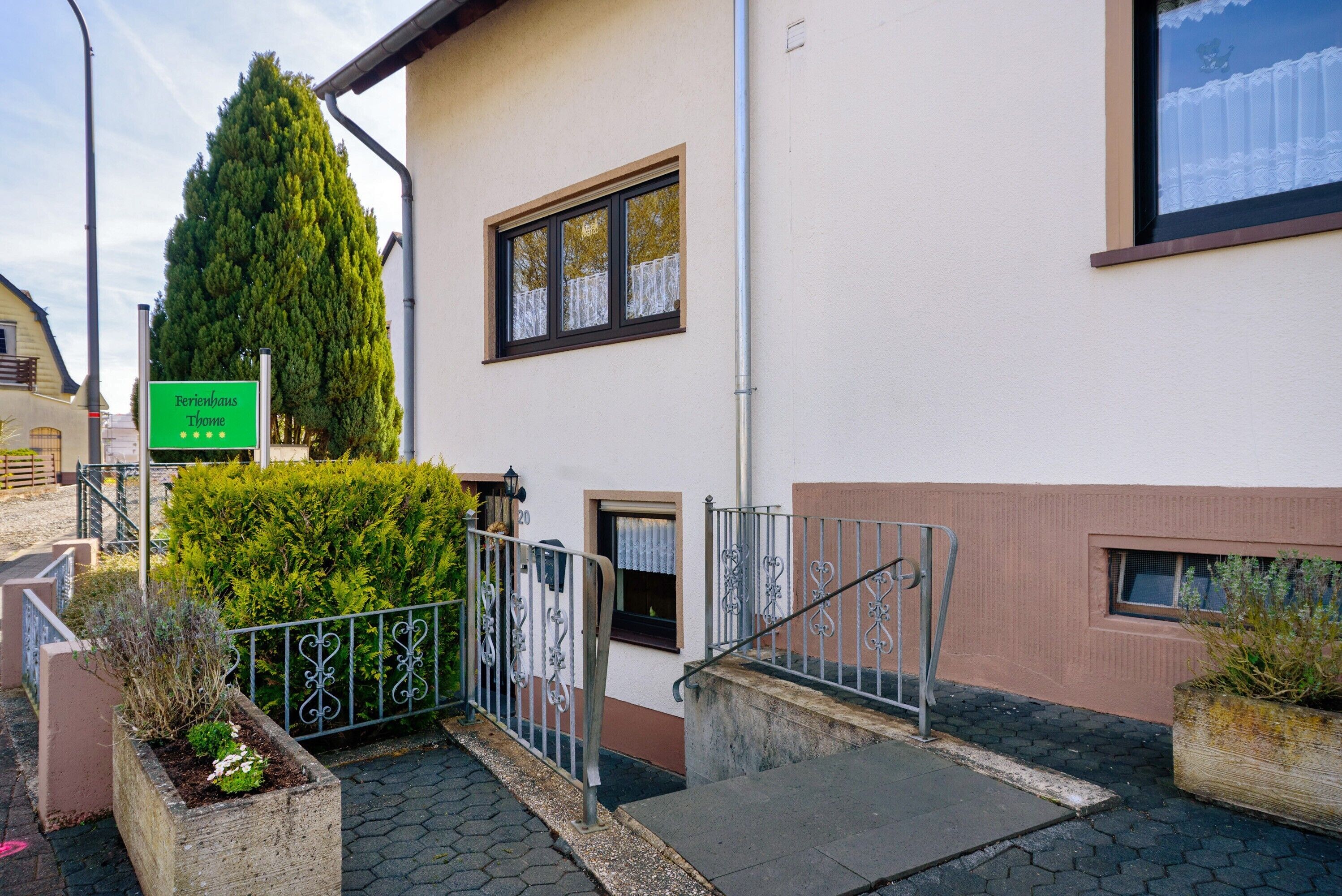 Un bâtiment avec une enseigne indiquant « Perihaus Thome », un escalier, une clôture en métal et un grand arbre.
