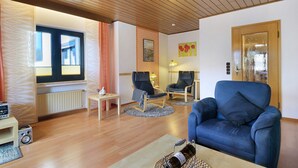 Una sala de estar con un sofá azul, dos sillones, una mesita y un radiador.