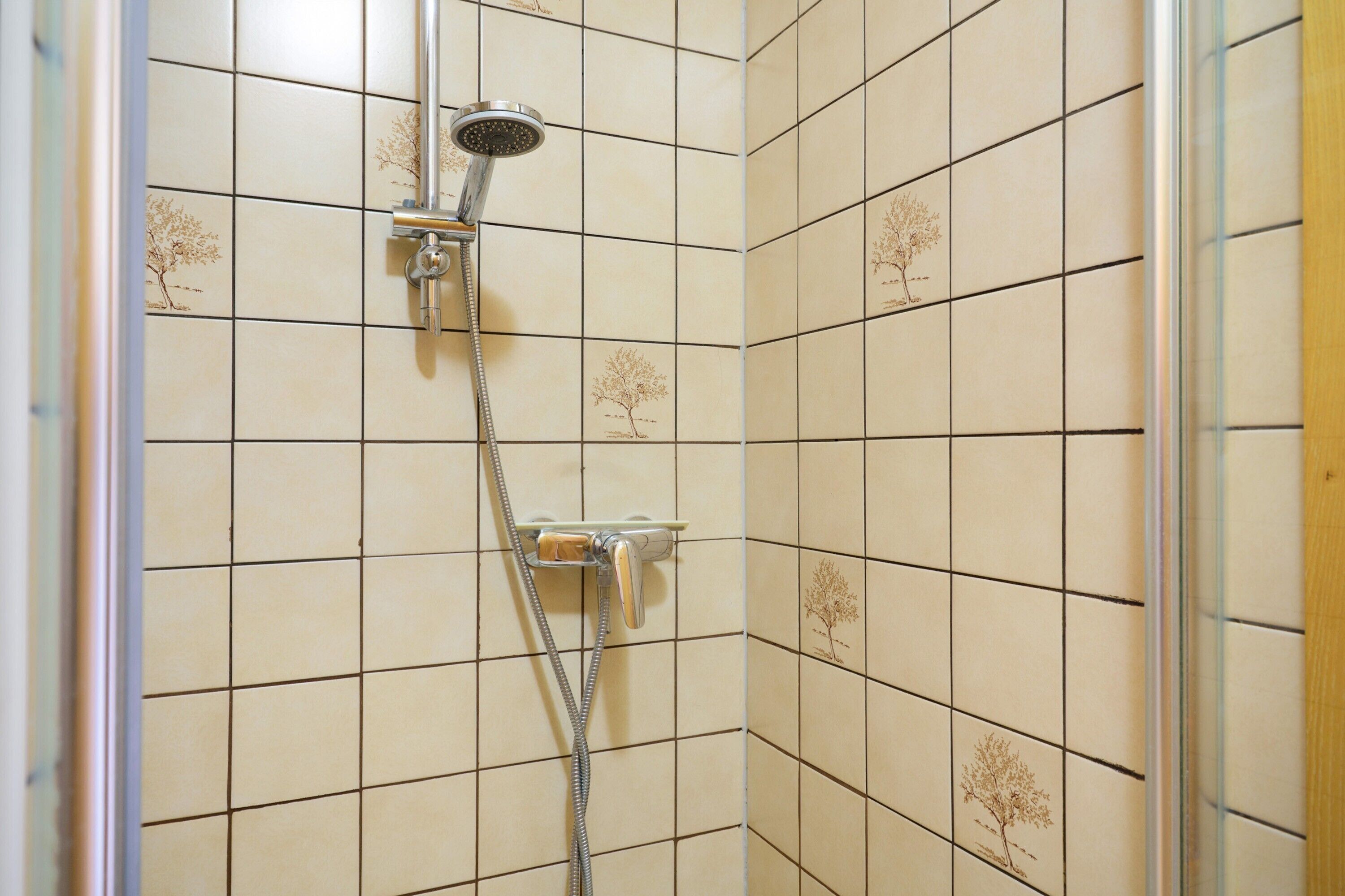 Eine Dusche mit Handbrause und verstellbaren Bedienelementen an der Wand.
