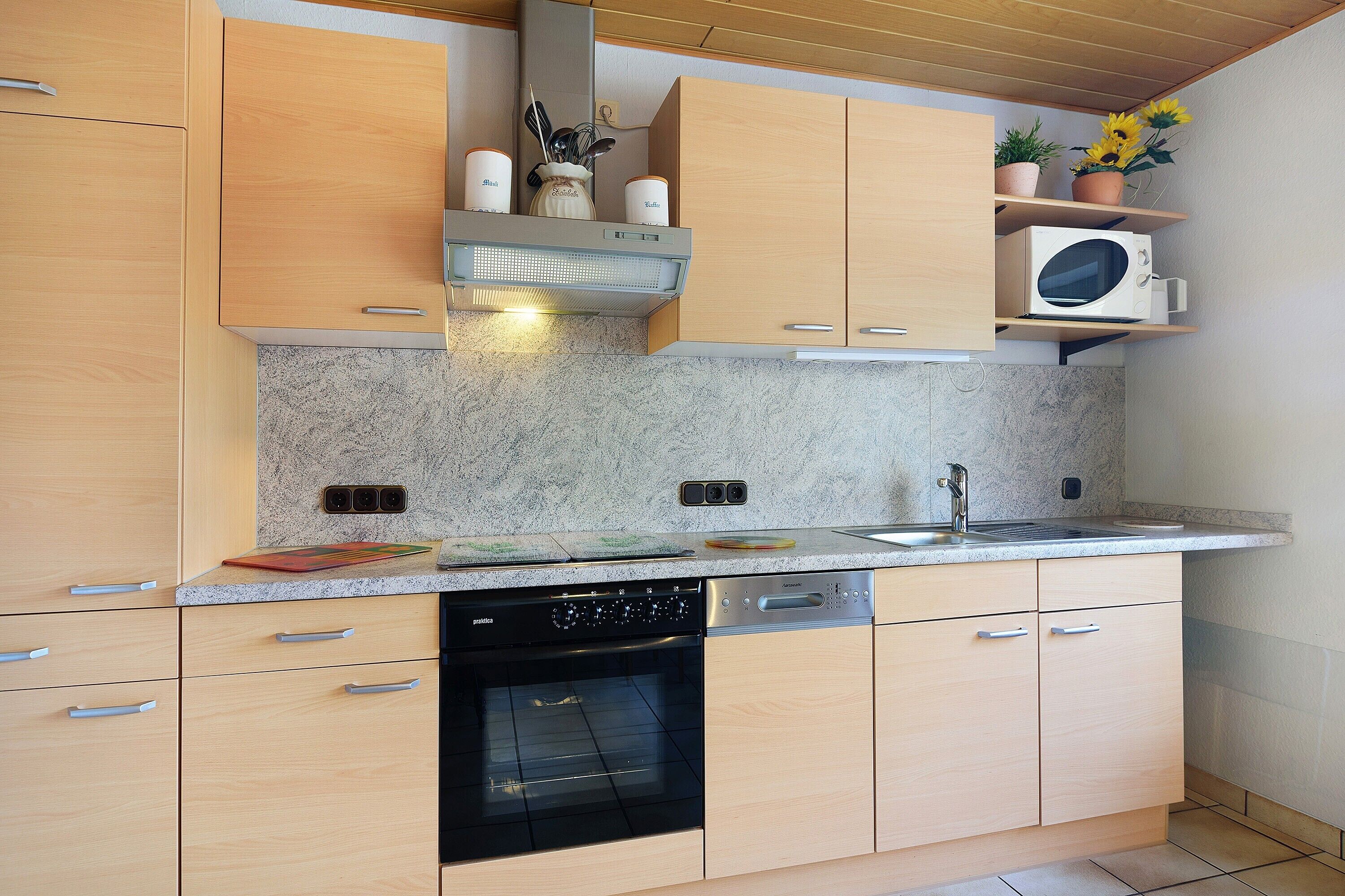 Une cuisine moderne avec des meubles en bois, un four encastré, un lave-vaisselle et un four à micro-ondes.