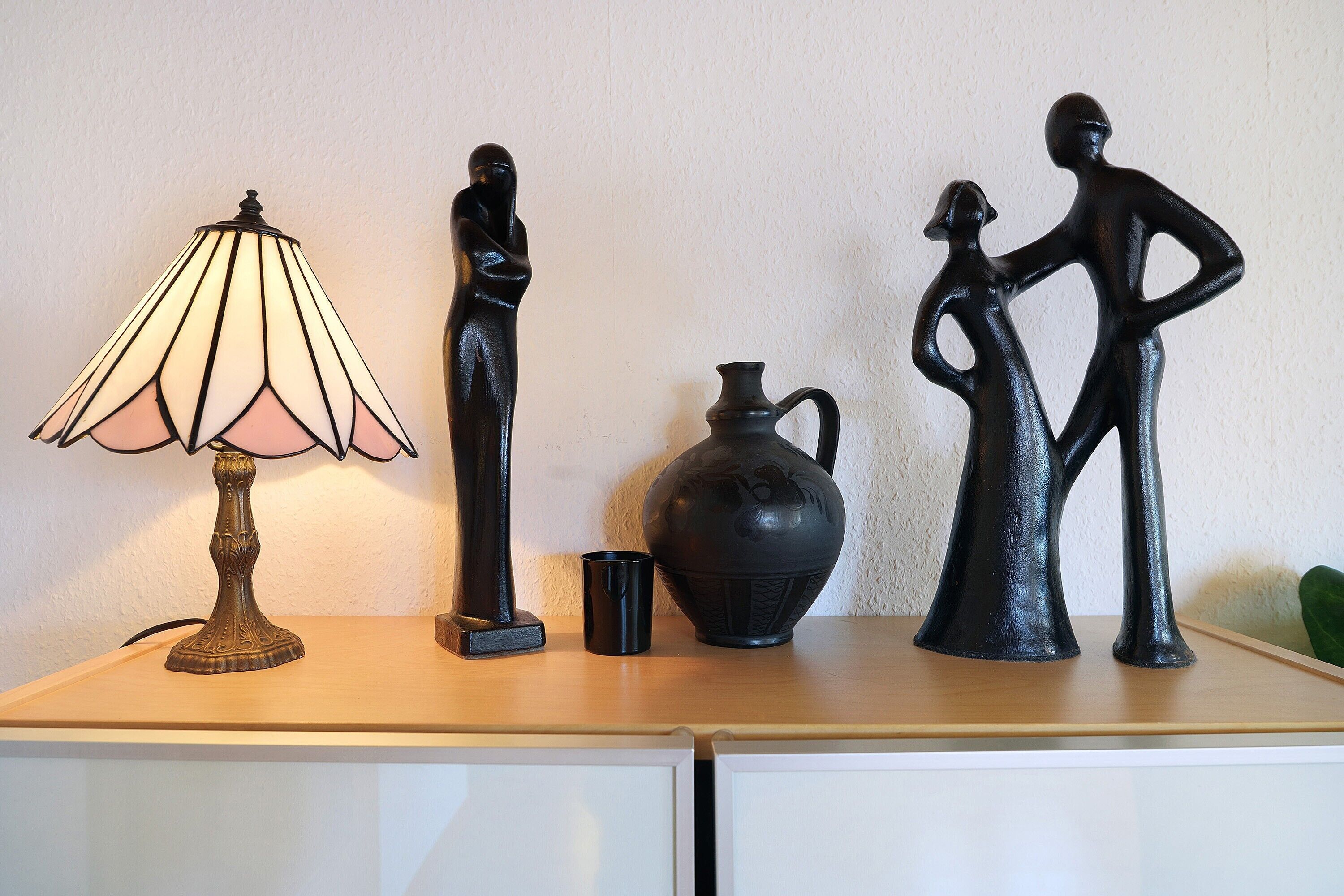 A table with a lamp, two black sculptures, and a black vase.