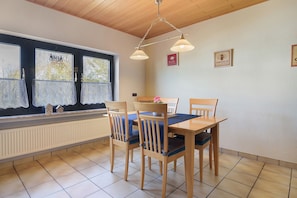 Un coin repas avec une table et des chaises, une fenêtre avec des rideaux et un radiateur.
