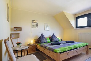 Une chambre avec un lit en bois, une petite table et une chaise, et une fenêtre.