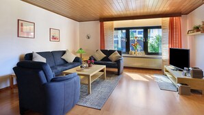Un salón con sofá, mesa de centro, televisor y ventana con cortinas.
