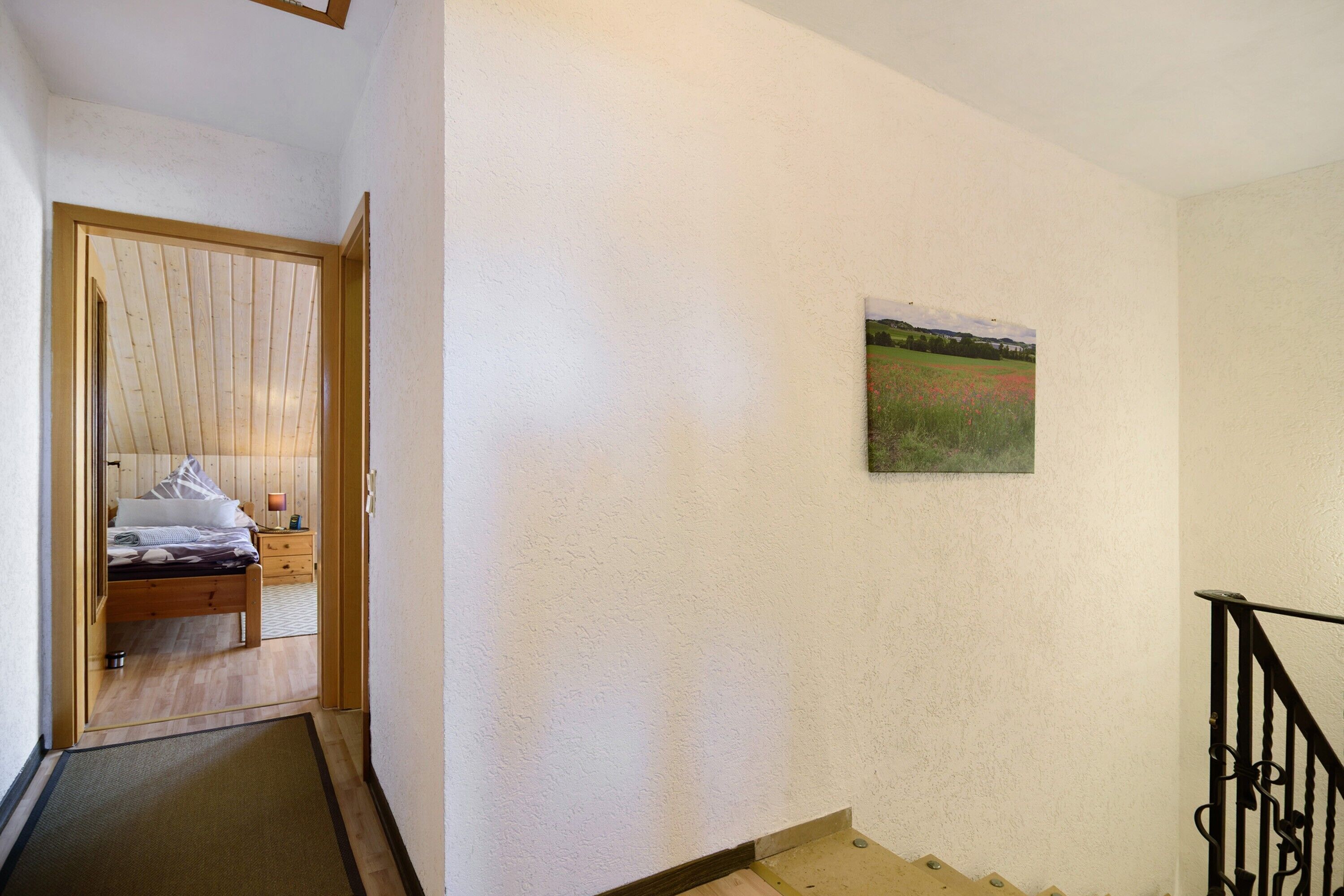 Un dormitorio con una cama, una mesita de noche, una lámpara y una puerta que da a otra habitación.