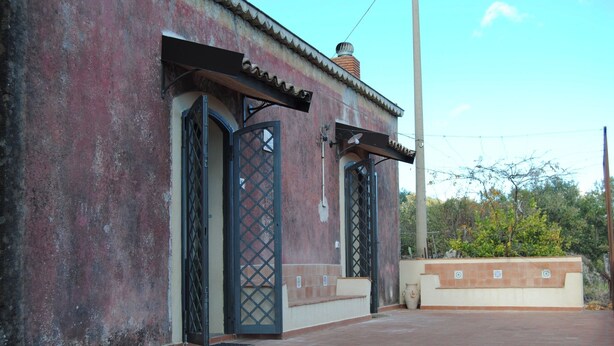Ein Gebäude mit verwitterter Fassade, zwei offenen Metalltoren und einer Pflasterterrasse.