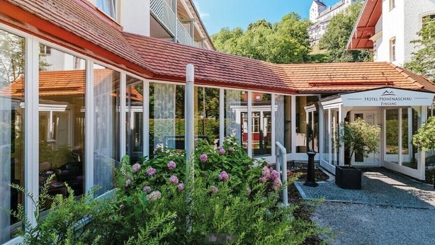 Um hotel com área externa coberta, paredes de vidro e um jardim com flores cor-de-rosa.