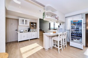 Een moderne keuken met witte kasten, een centraal eiland, een koffieapparaat en een automaat voor drankjes.