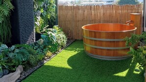 Un jardin sur le toit doté d’un bain à remous en bois, d’une pelouse artificielle et de diverses plantes.
