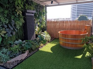 Um jardim no terraço com grama sintética, um barril de madeira e diversos tipos de plantas.