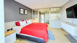 Une chambre à coucher moderne avec un lit, des tables de chevet, une télévision et une grande fenêtre.