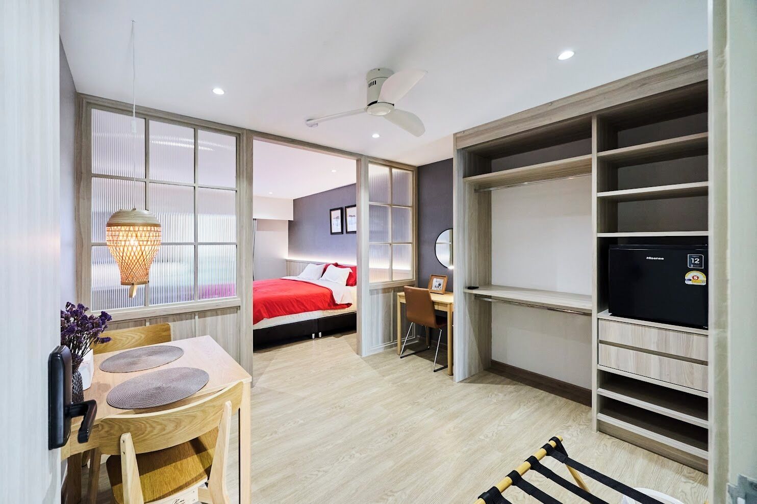 A hotel room with a bed, a desk, a chair, a dining table, a lamp, and a wardrobe.