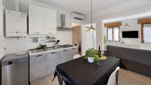 A modern kitchen with a built-in stove, a sink, and a dishwasher. There is a dining area with a table and chairs, and a large window with curtains. - Apartment 'Ca' Mirabello' with Wi-Fi and Air Conditioning (Bardolino)