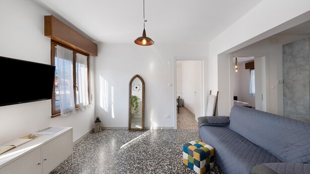 A modern living room with a flat-screen TV, a sofa, a colorful ottoman, and a pendant light. - Apartment 'Ca' Mirabello' with Wi-Fi and Air Conditioning (Bardolino)