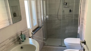 Un bagno moderno con un lavandino ampio, due servizi igienici, una cabina doccia in vetro e uno specchio illuminato.